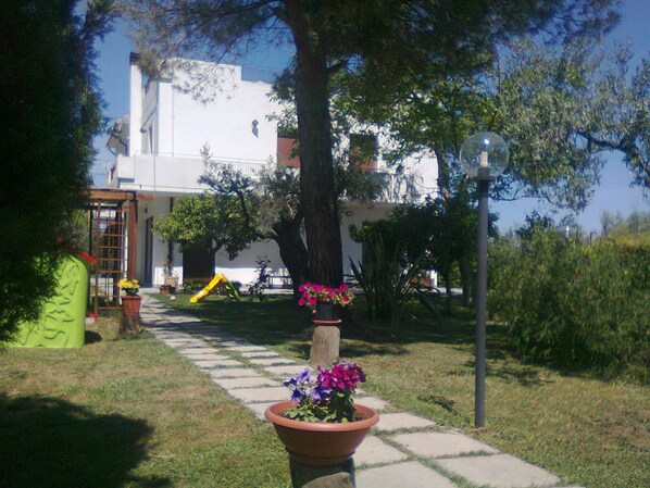 A pathway leading to a white building with a large tree and a playground in the background. - B&B dal Barbarossa (Vasto)