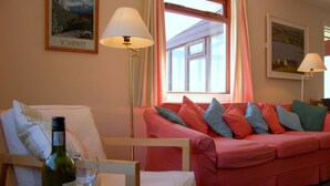 A cozy living room with a pink sofa, a wooden chair, and a table with a wine bottle and glass.
