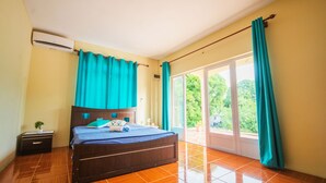 Une chambre à coucher avec un lit en bois, une table de chevet, une fenêtre avec des rideaux et une vue sur la verdure à l’extérieur.