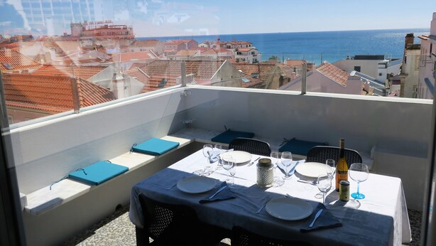 A balcony with a table set for dining, overlooking a coastal cityscape.