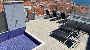 A rooftop terrace with a swimming pool, lounge chairs, and a view of the city and sea.