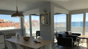 A modern apartment with a dining area, a living space with a sofa and a table, and large windows offering a view of the cityscape.