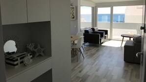 A modern living room with a balcony, a dining area, and a view of the sea.
