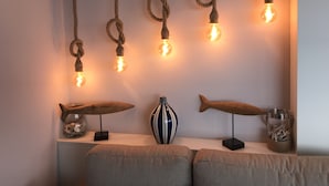 A room with a white wall, a wooden shelf with decorative items, and a hanging light fixture with exposed bulbs.