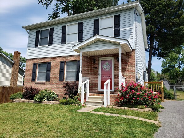 A two-story house with a brick facade, a front porch, and a welcome sign.