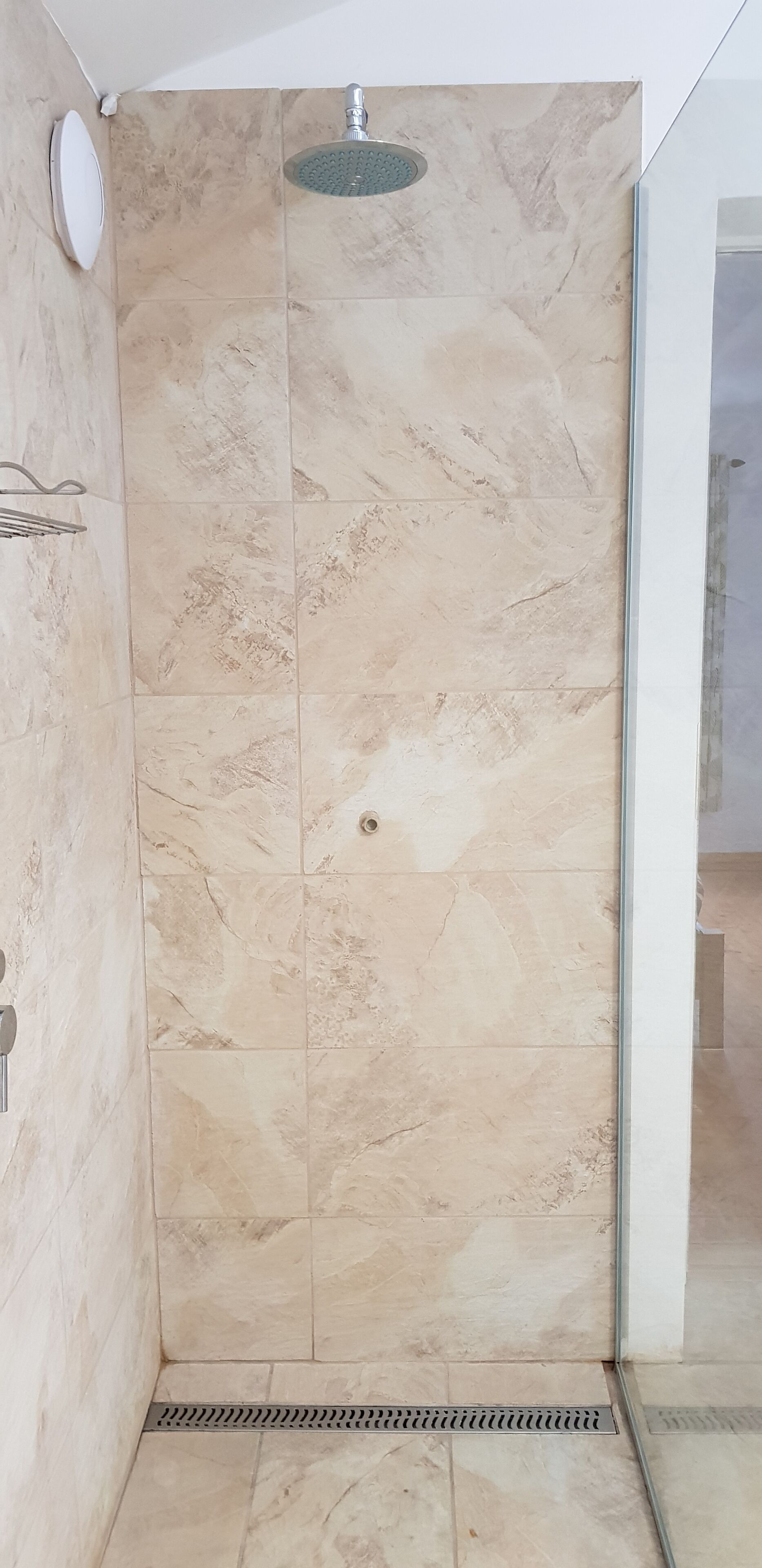 A shower area with beige marble tiles and a glass door.