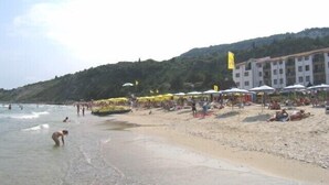 A beach with umbrellas and people. There is a building with multiple floors in the background. - Beautiful villa, stunning views, great location (Kranevo)