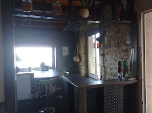 A compact kitchen with a stone wall, a window, and a bar area with bottles.
