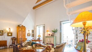 Un soggiorno spazioso con soffitto alto, arredi in legno e un'ampia finestra che lascia entrare la luce naturale.