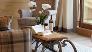A cozy living room with a plaid sofa, a wooden coffee table with a book and a bottle of wine, and white orchids. - High-quality apartment with a private sauna and a dream view right on the ski slope (Westendorf)