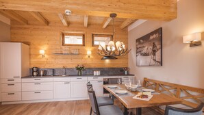 A modern kitchen with wooden beams, a dining area with a wooden table and chairs, and a wall-mounted light fixture. - High-quality apartment with a private sauna and a dream view right on the ski slope (Westendorf)