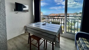A balcony with a table and chairs, a TV mounted on the wall, and a view of the sea and buildings. - Saint-Cyprien Rental: 2-room apartment with parking, terraces, and loggia (Saint-Cyprien)