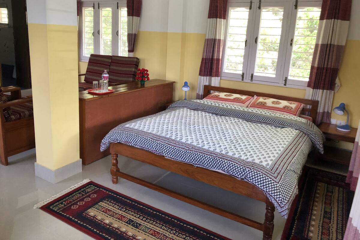 A bedroom with a wooden bed, a desk, a chair, and a window with curtains.