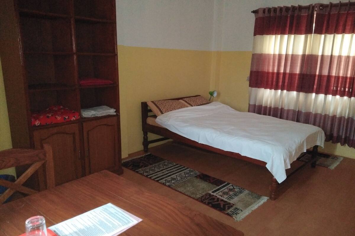 A room with a single bed, a wooden desk, a bookshelf, and a patterned rug.