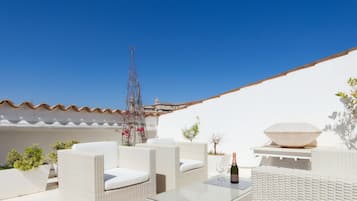A rooftop terrace with wicker furniture, a large decorative bowl, and a bottle of champagne.