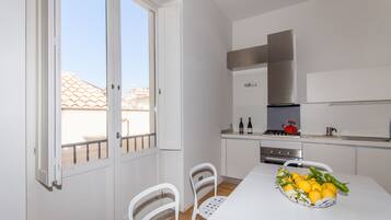 A modern kitchen with white cabinets, a stainless steel range hood, and a dining area with a table set for two.