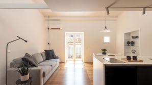 A modern living space with a sofa, a small side table with a plant, a pendant light, and a kitchen area with a countertop and shelves. - Kalsa miniLoft by Wonderful Italy (Palermo)