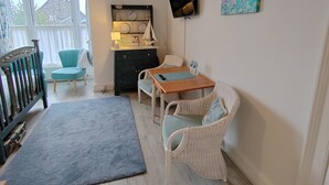 A cozy room with a wooden table, wicker chairs, a blue rug, a dark dresser, and a painting of a seascape. - Puddle Duck Lodge (Windermere)