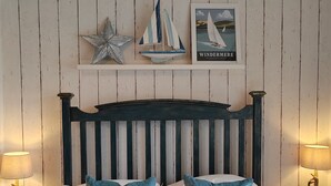 A bed with a dark headboard, two pillows, a framed picture of a sailboat, and a star decoration on the wall. - Puddle Duck Lodge (Windermere)