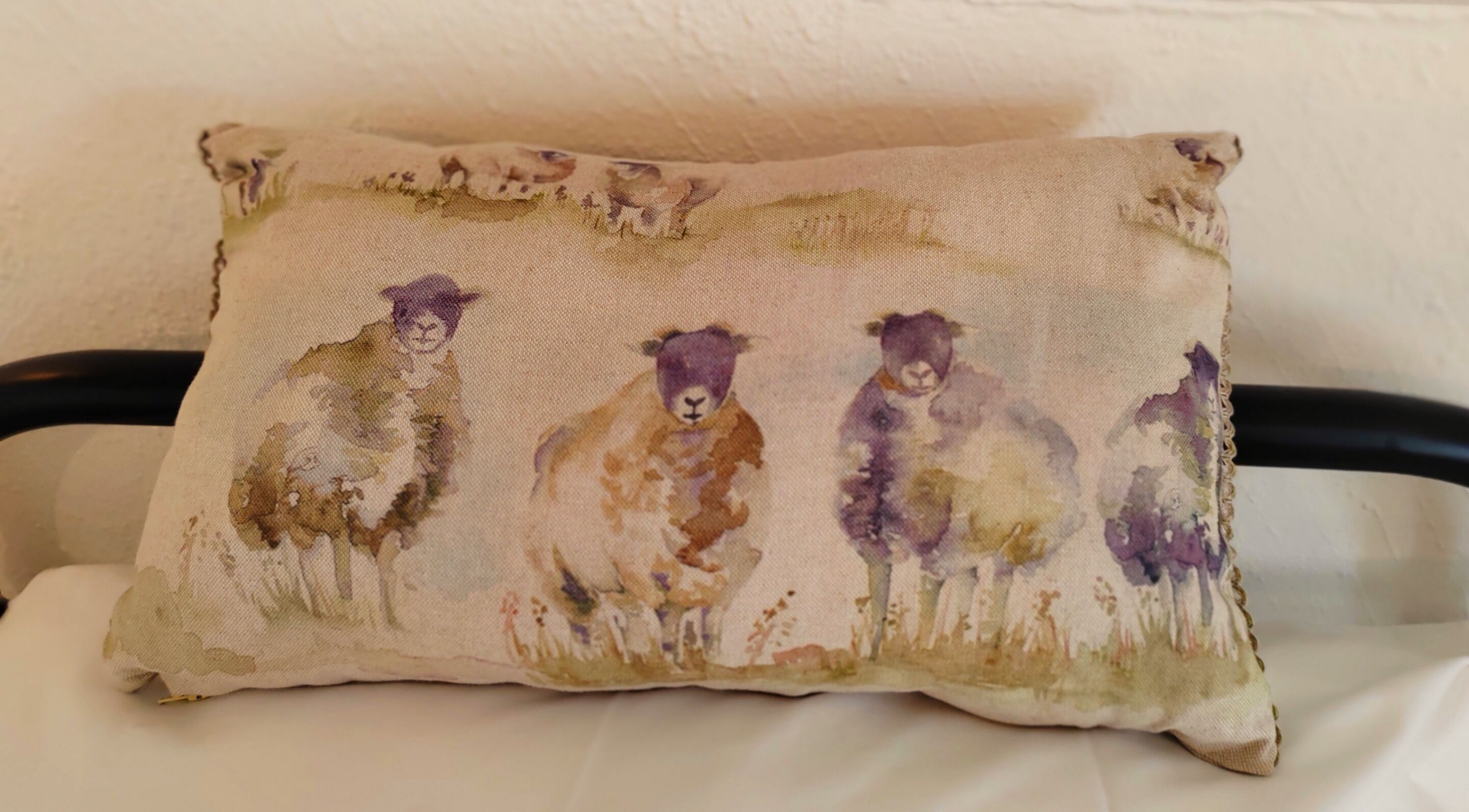 Almohada con una escena campestre que muestra ovejas.