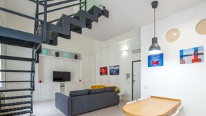 Una sala moderna con un sofá gris, una mesa de madera, un televisor y una escalera.