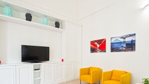 Una sala de estar moderna con un televisor de pantalla plana, dos sillones amarillos, armarios blancos y dos cuadros en la pared.