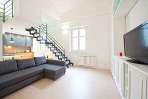 A modern living room with a grey sectional sofa, a staircase, a kitchen area, and a TV on a white cabinet. - Loft 18 by Wonderful Italy (Palermo)