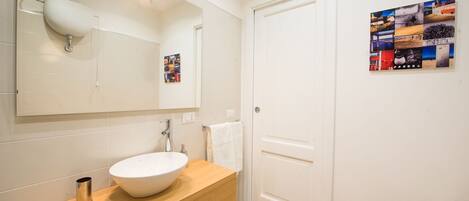 A bathroom with a white sink, wooden vanity, and a large mirror. There is a towel rack and a door with a poster on the wall.