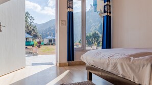 A bedroom with a bed, a view of a mountainous area, and a door leading to an outdoor area with tables and chairs. - Blossom Bliss Resort (Dhari)
