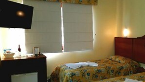 A hotel room with two beds, a TV, a desk with a lamp, and a window with blinds. - Pousada Sonnenhof (Gramado)