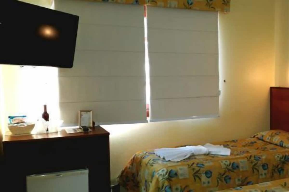 A hotel room with two beds, a TV, a desk with a lamp, and a window with blinds.