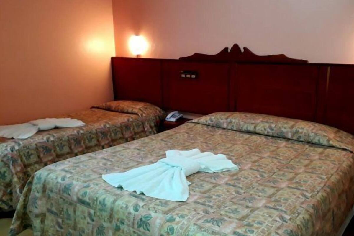 A hotel room with two beds, each with floral-patterned bedding and a white towel on one bed.