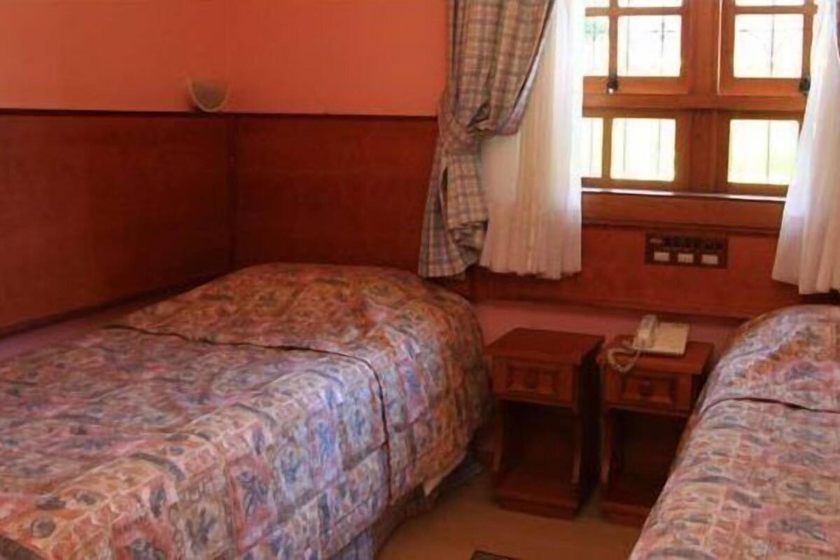 A room with two single beds, a small wooden nightstand, and a window with curtains.