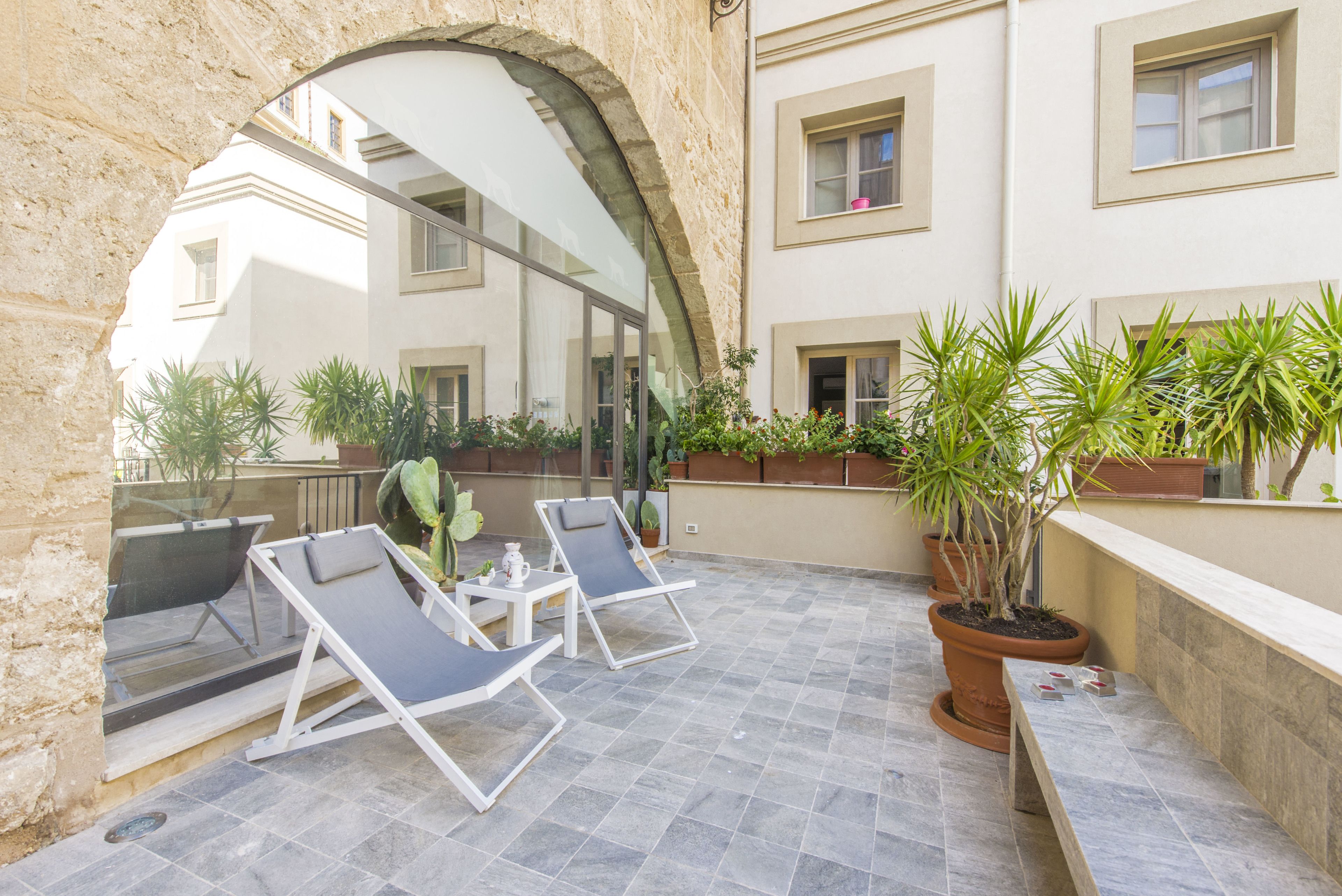 Un patio al aire libre con sillones de descanso, plantas en macetas y un arco de piedra.