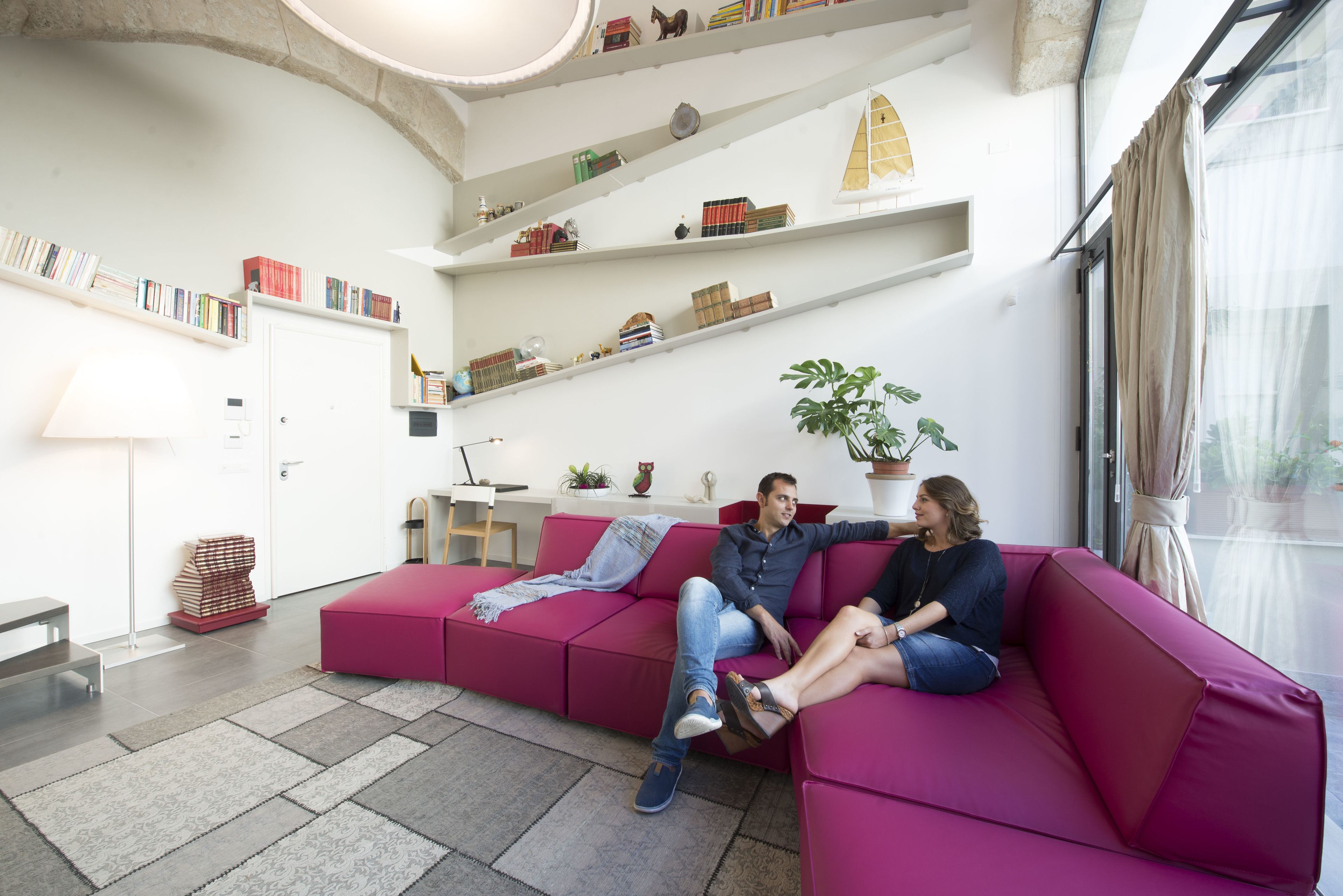 A modern living room with a pink sectional sofa, a bookshelf with various items, and a potted plant.