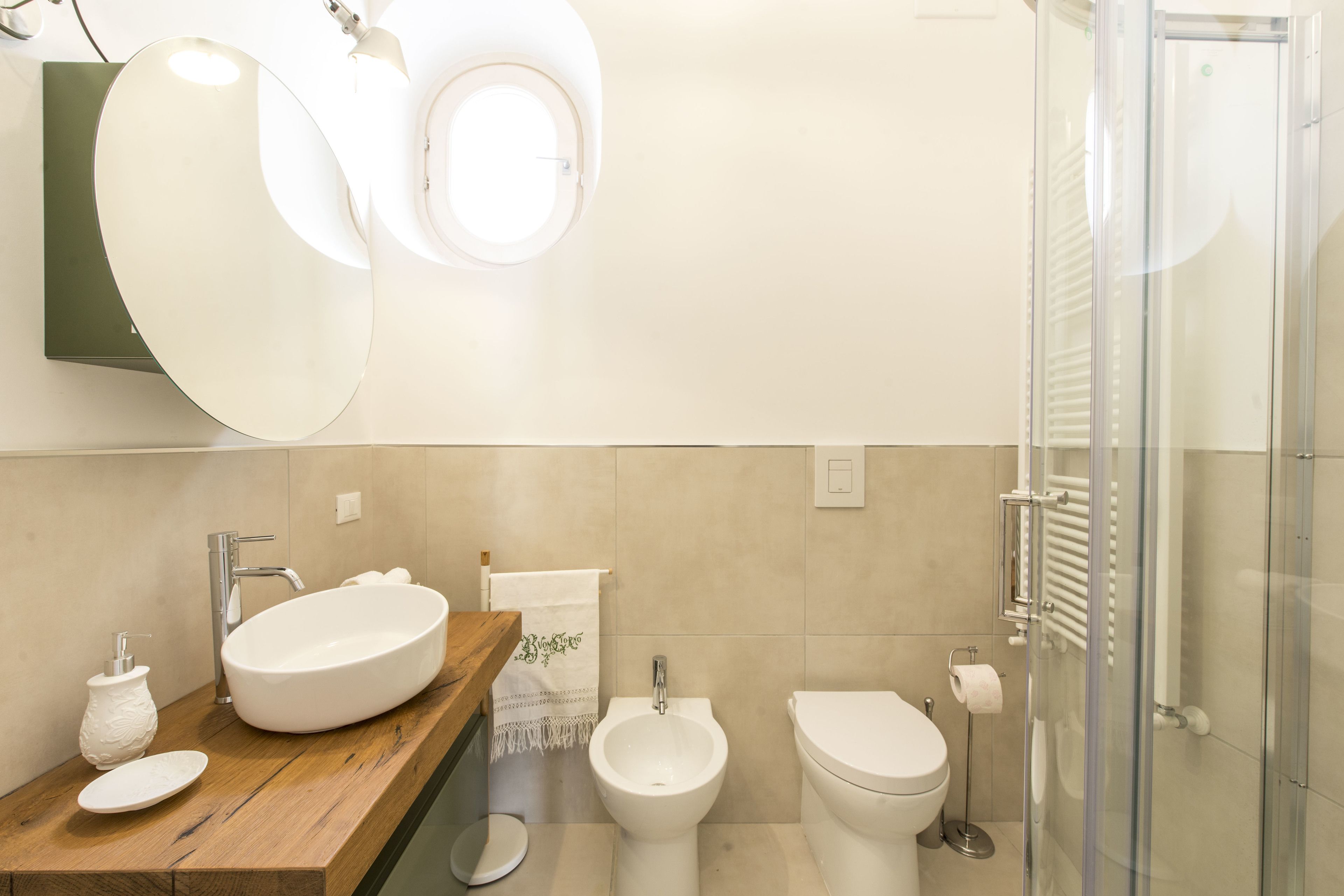 A modern bathroom with a wooden vanity, a large oval sink, a bidet, a toilet, and a glass shower enclosure.