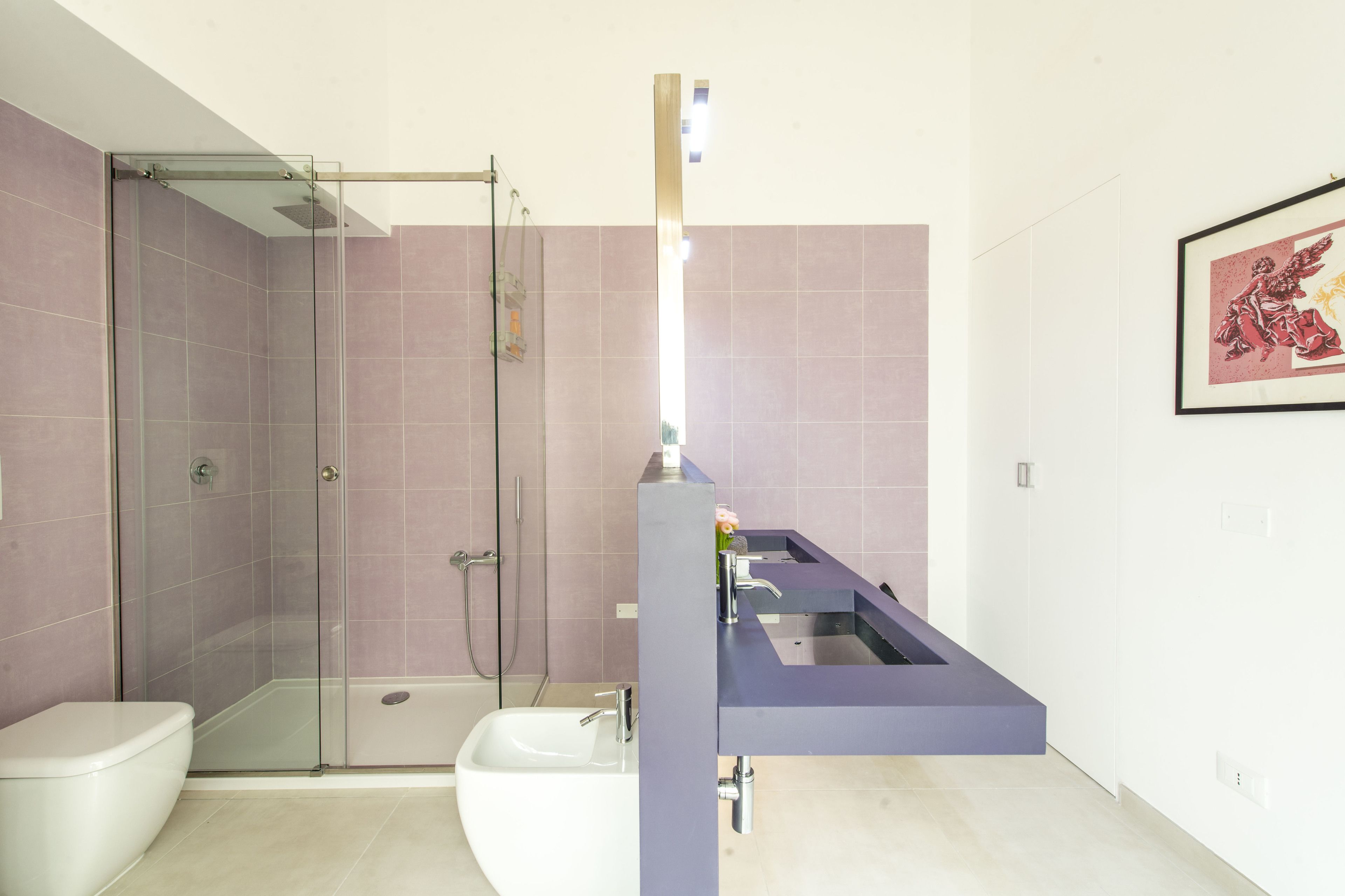 Et moderne badeværelse med en brusekabine i glas, et hvidt toilet og en vask med en lilla bordplade.