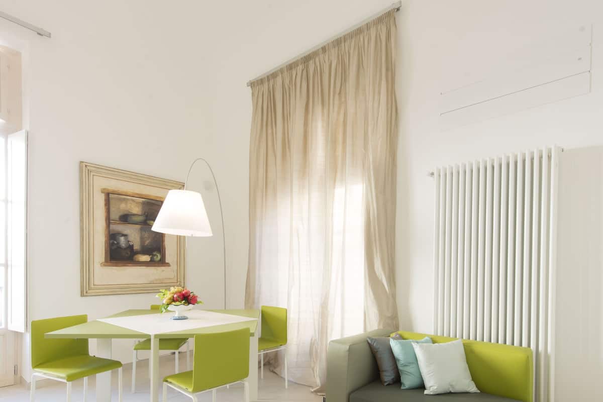 A bright, well-lit room with a dining table, chairs, a sofa, and a radiator.