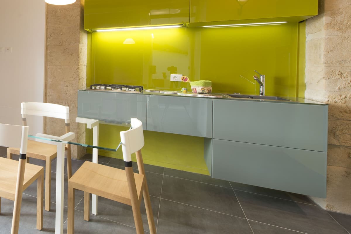 A modern kitchen with a green backsplash, wooden ceiling beams, and a dining area with a glass table and chairs.