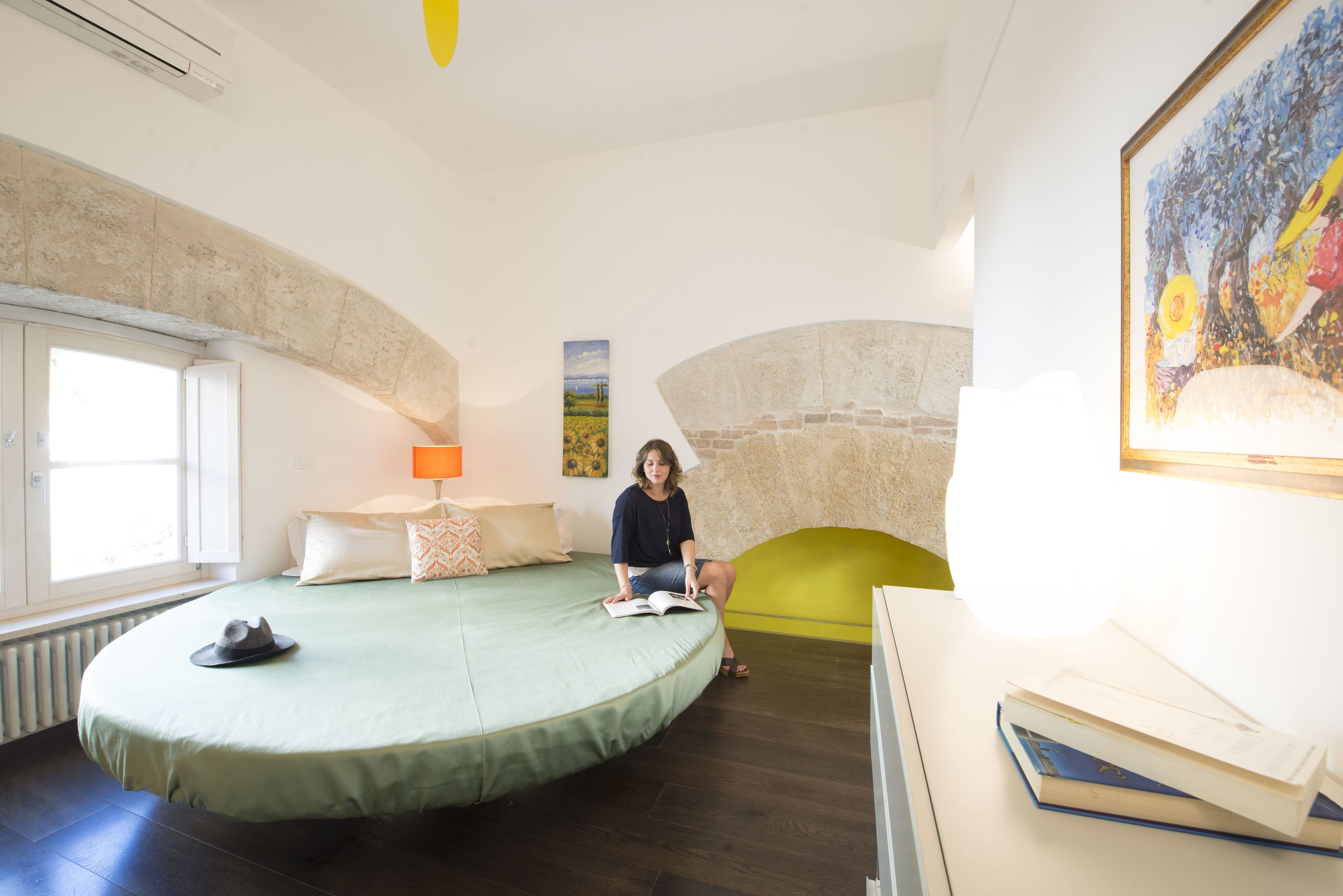 Une pièce avec un lit à la forme arrondie, une fenêtre, une lampe et un tableau accroché au mur.