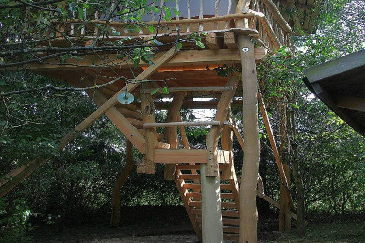 A wooden treehouse with a staircase and a platform, surrounded by trees.