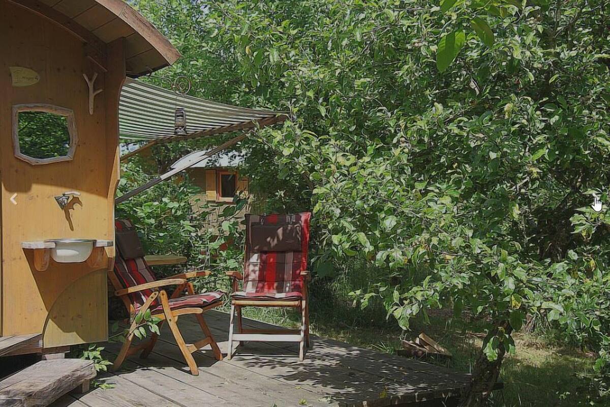 A wooden deck with two rocking chairs and a small table, surrounded by lush greenery.