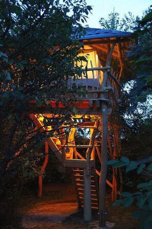 Ein Baumhaus mit einer Holztreppe, die zu einer Plattform mit Dach führt.