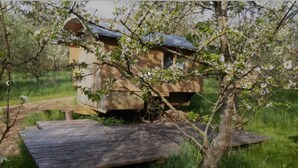 A wooden structure with a sloped roof, possibly a cabin or shed, surrounded by lush greenery and a wooden deck. - Schaeferwagenhotel-Campsite (Sulzfeld)