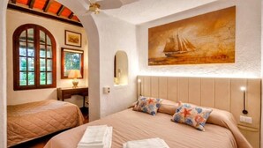 A bedroom with a bed, two pillows, a nightstand, a lamp, a painting, and a window.
