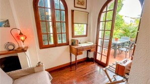 A room with a wooden desk, a bed, and large arched windows.