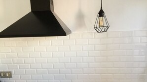 Uma cozinha com coifa preta, tábua de corte de madeira e painel de tijolos brancos.