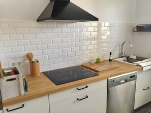 Eine moderne Küche mit weißen, im Zickzackmuster angeordneten Fliesen, einer schwarzen Dunstabzugshaube, einer Holz Arbeitsplatte, einem eingebauten Geschirrspüler und einem Holz-Küchenhelfer-Halter.