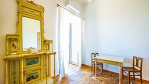 A room with a wooden floor, a large ornate mirror, a white table, two wooden chairs, and a door leading outside. - Amazing Sea View in Historic Building in Downtown by Wonderful Italy (Palermo)