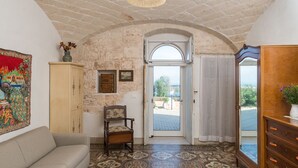 Una habitación con techo de piedra, piso estampado, un sofá, una silla de madera, un armario y vistas a través de una puerta.